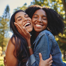 Two friends smiling while hugging outside