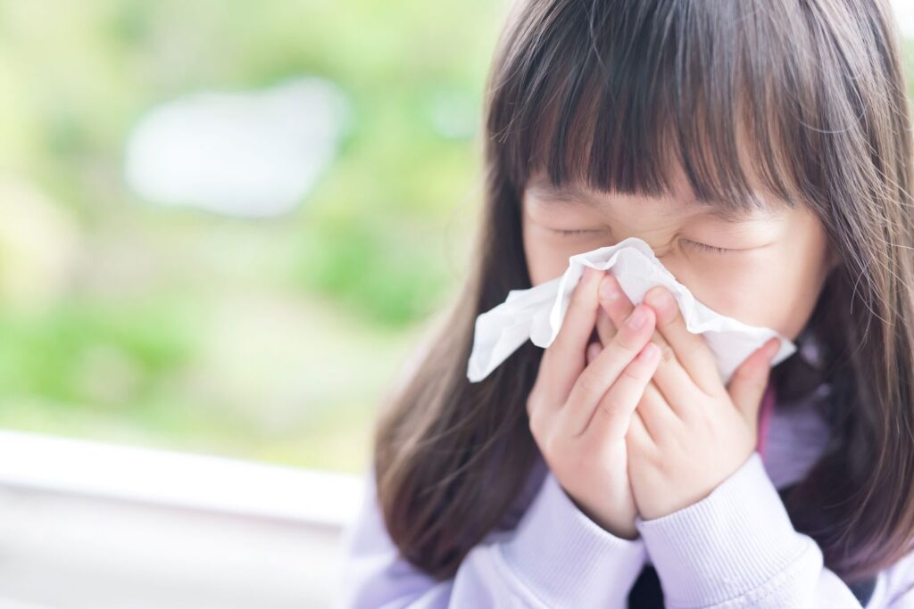 LIttle girl with long brown hair blowing her nose into tissue