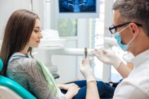 Young woman talking to dentist holding a dental implant post. 