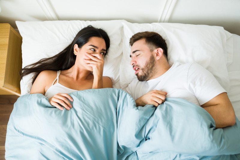 Woman lying next to sleeping man while covering her nose