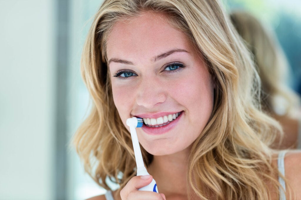 Happy-blonde-brushing-her-teeth-in-the-bathroom-at-home
