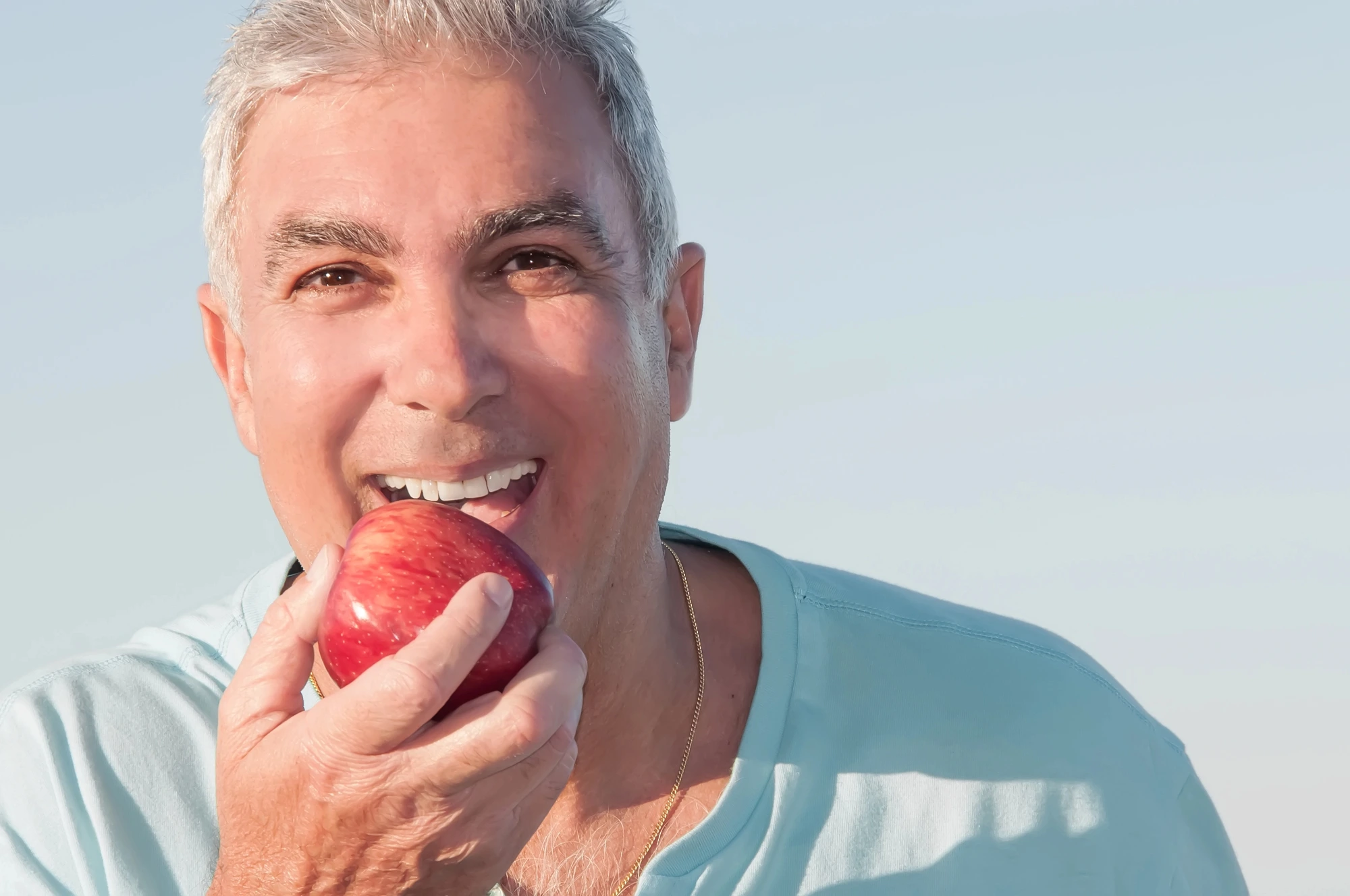 happy man eating apple after getting dentures in Henrico
